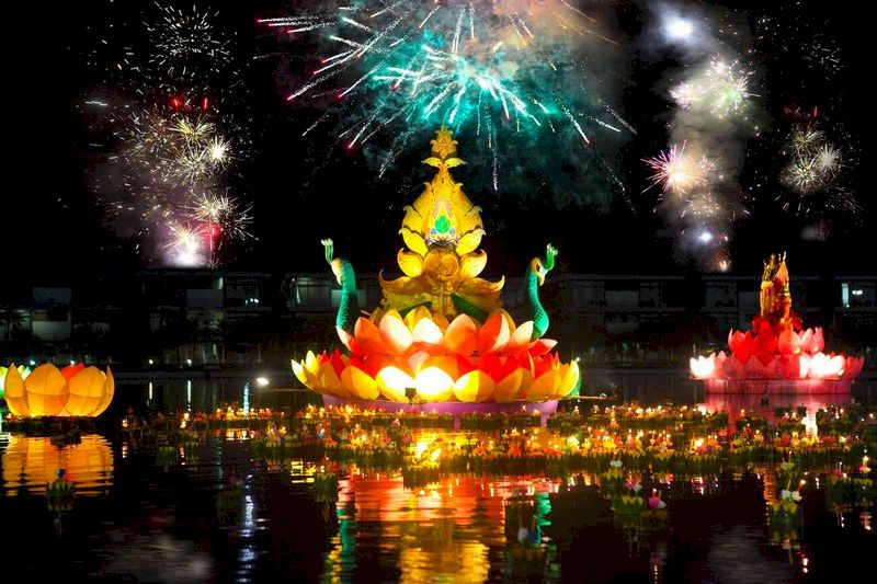 Armonía luminosa Krathong de diferentes tamaños flotando bajo fuegos artificiales.