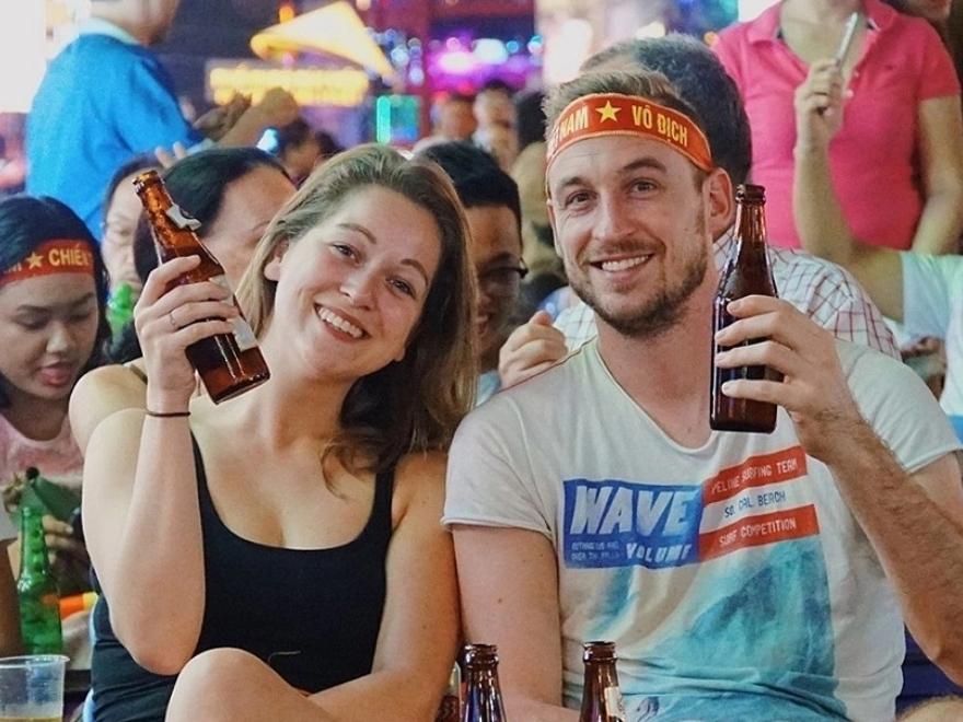 Travelers and locals sitting on plastic stools enjoying cold bia hoi at Ta Hien Beer Street in the evening.