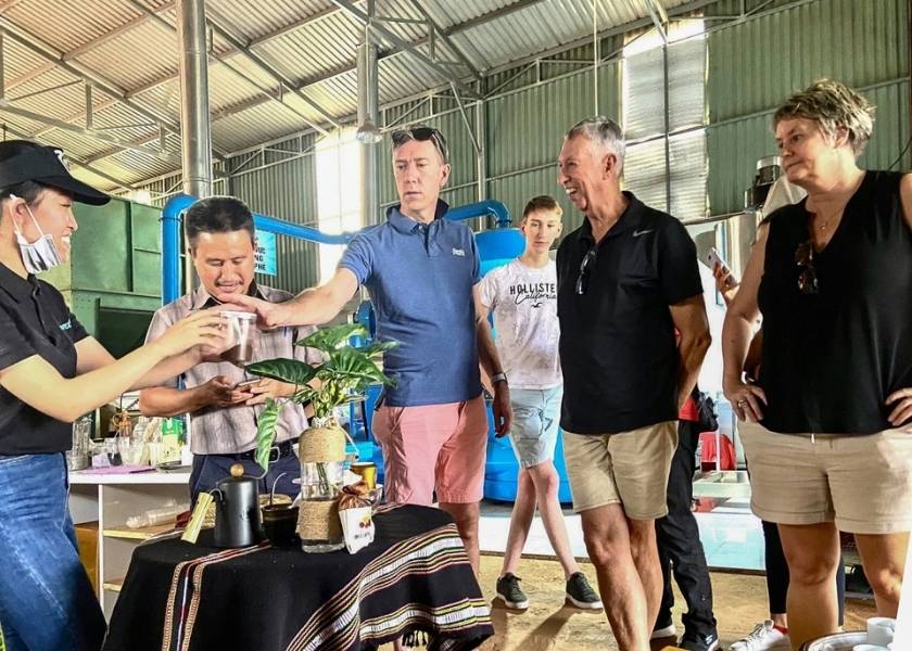 A group of Western tourists observing and tasting coffee at a processing facility in Buon Ma Thuot, Vietnam.