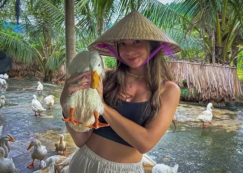 A Western girl smiling while holding a white duck gently at the Duck Stop in Phong Nha, Vietnam.