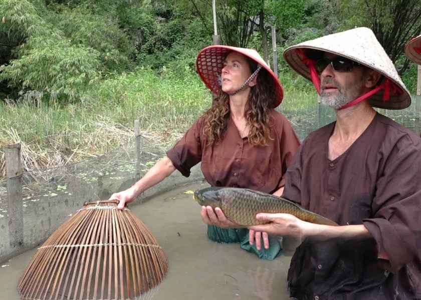 Western tourists wearing traditional 'Ao Ba Ba' catch fish in Vinh Long, Mekong Delta, Vietnam.