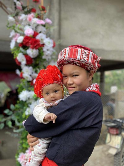 A mother and her baby, both dressed in colorful Mong wedding attire